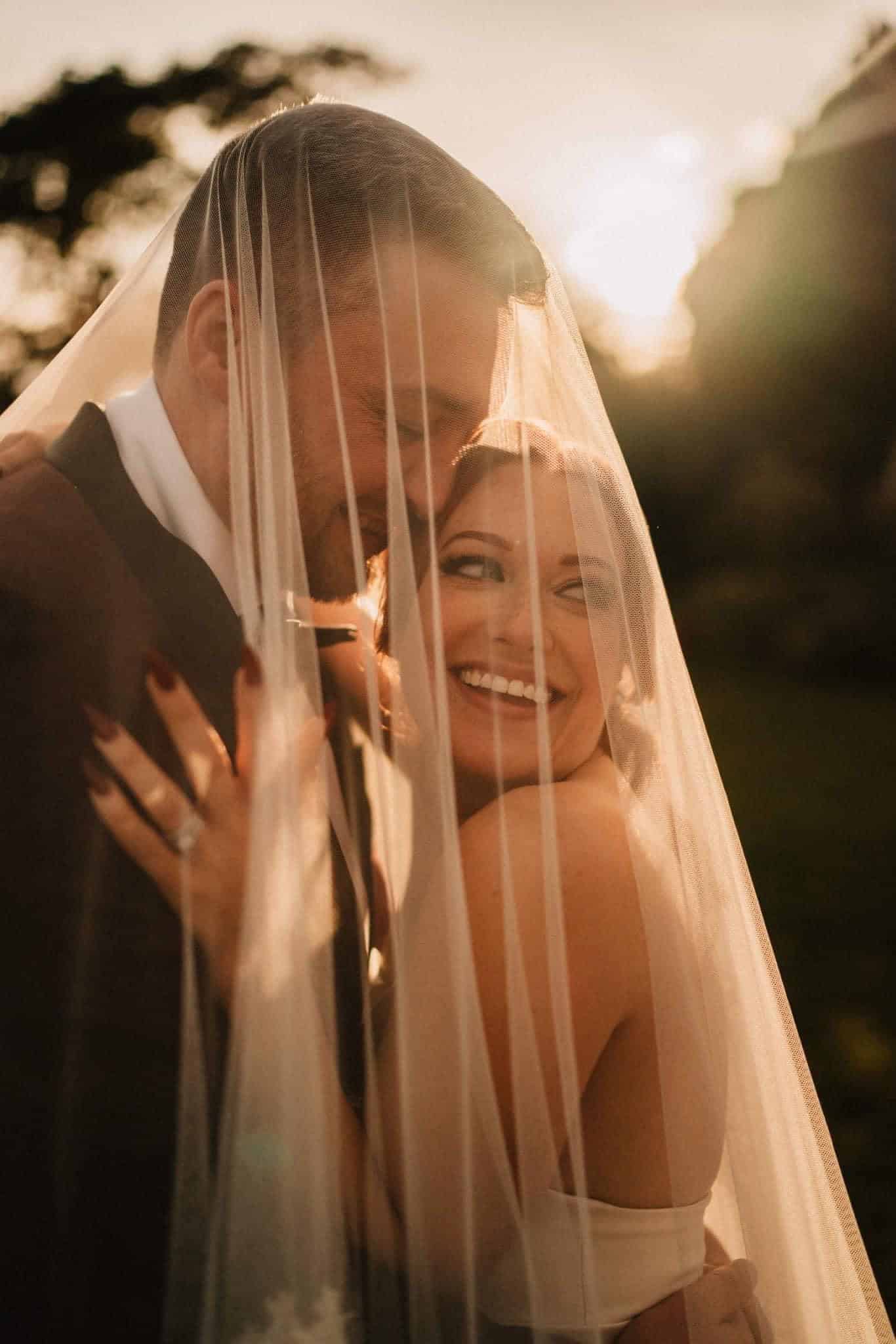 Bride snuggled into the groom smiling over her shoulder at sunset