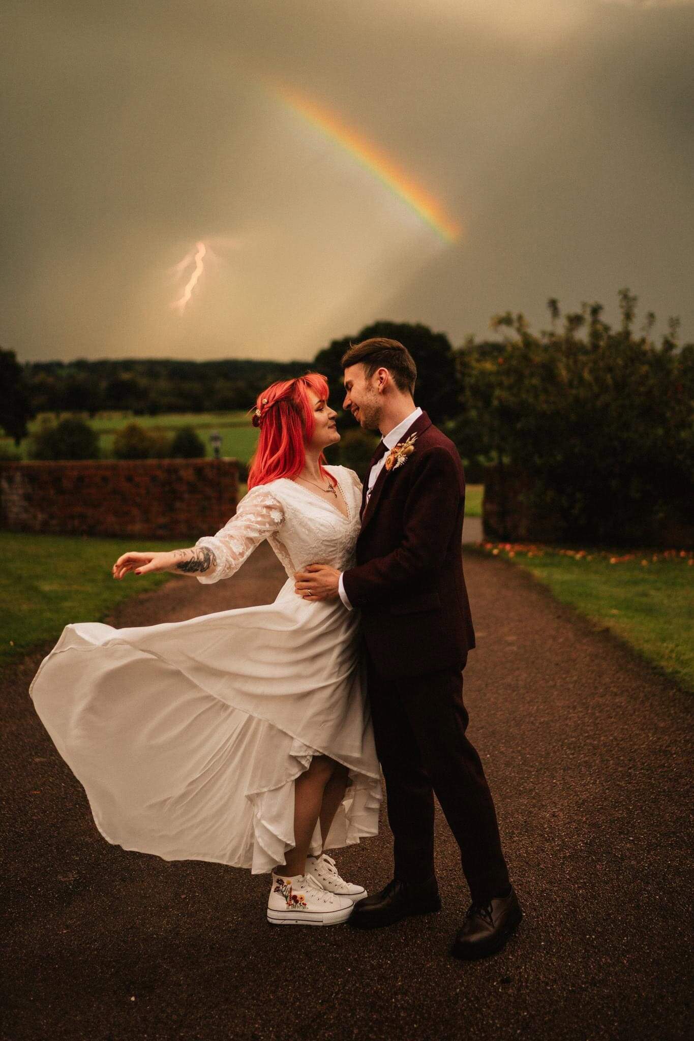 Boho bride with the dress flicking out during a thunderstorm with a rainbow stood with her groom